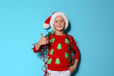 Photo of Cute little boy in handmade Christmas sweater and hat with streamers on color background