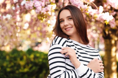 Beautiful woman near blossoming tree on spring day, space for text