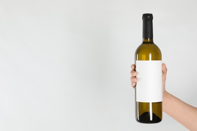 Woman holding bottle of white wine on light background, closeup. Space for text