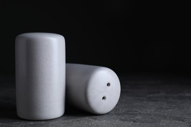 Photo of Salt and pepper shakers on dark textured table, closeup. Space for text