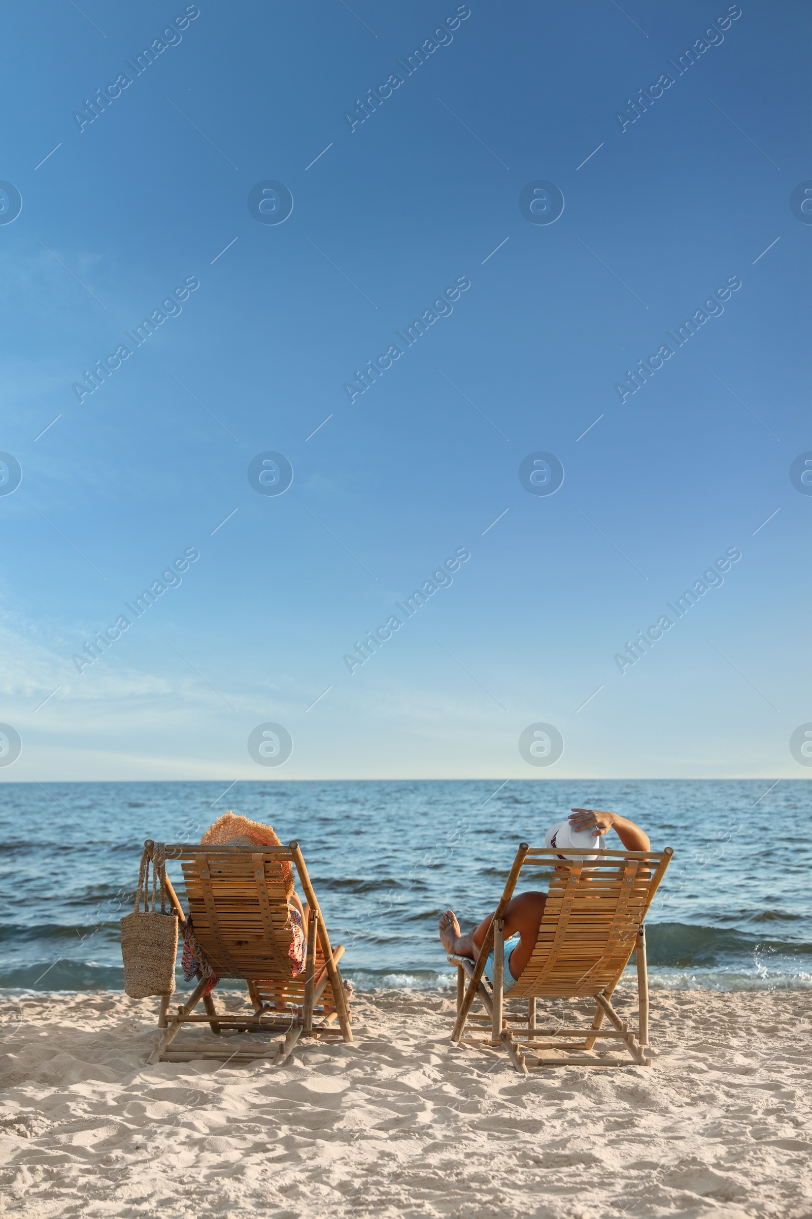 Photo of Young couple relaxing in deck chairs on beach near sea