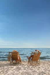 Young couple relaxing in deck chairs on beach near sea