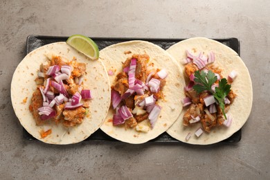 Delicious tacos with vegetables, meat and lime on grey textured table, top view