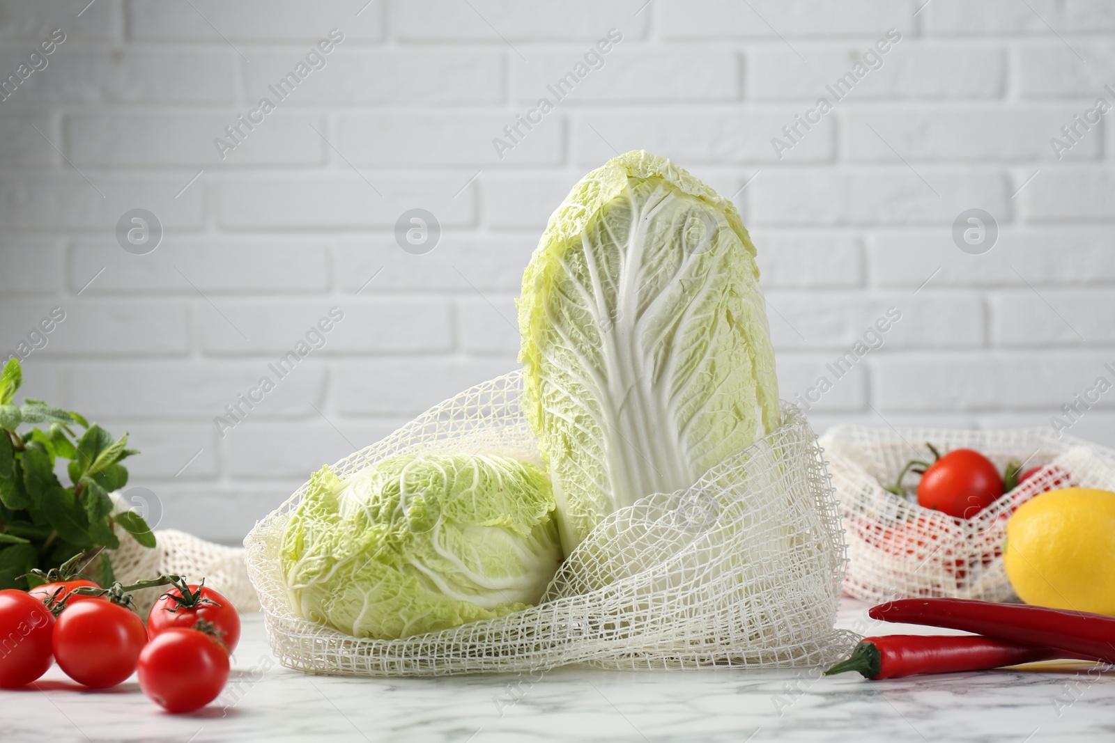 Photo of Fresh Chinese cabbages and other vegetables on white marble table near brick wall