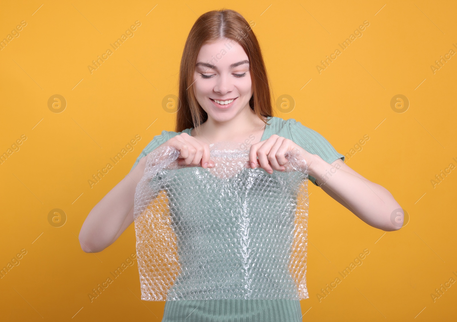 Photo of Woman popping bubble wrap on yellow background. Stress relief