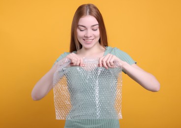 Woman popping bubble wrap on yellow background. Stress relief