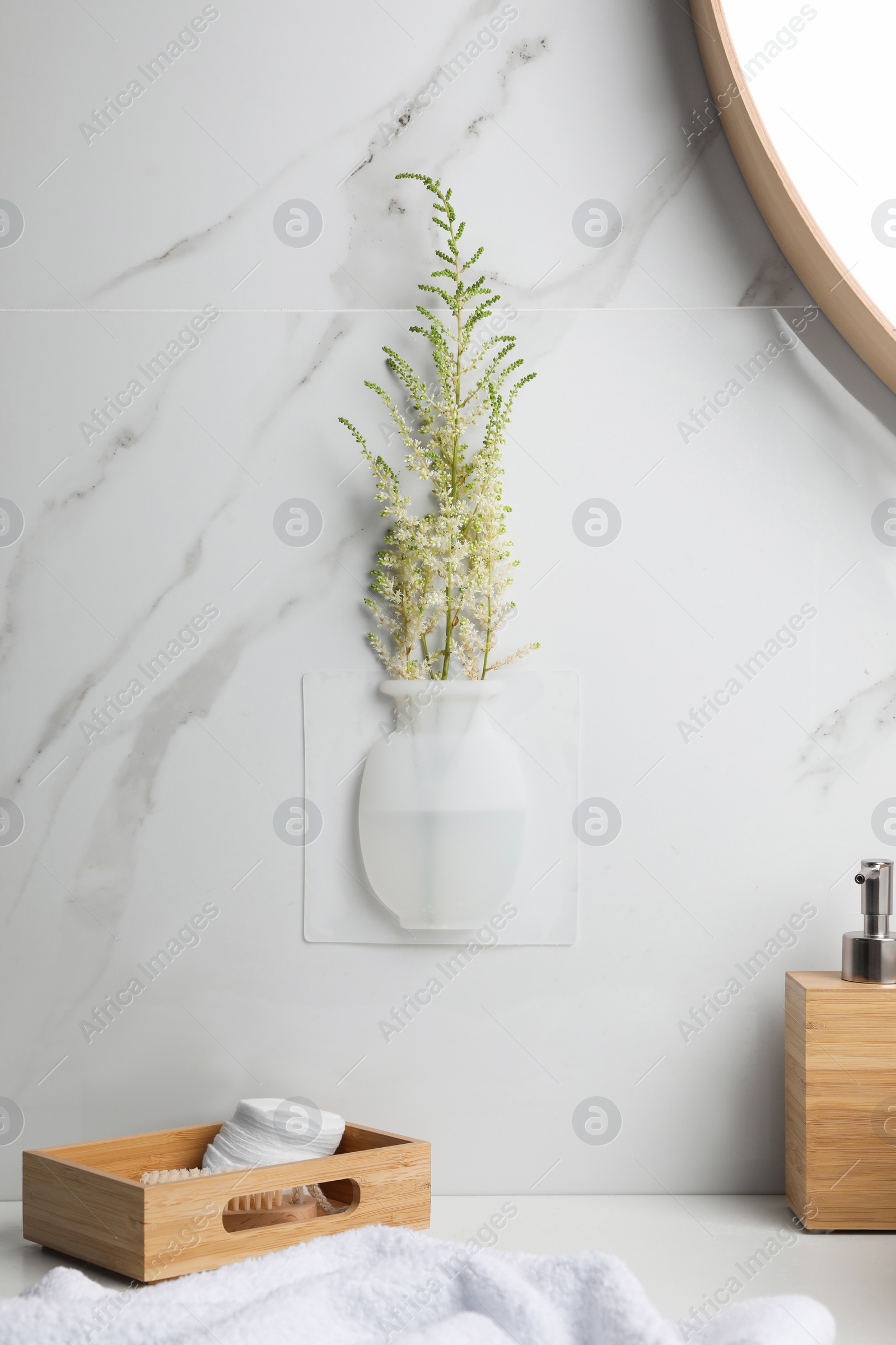 Photo of Silicone vase with flowers on white marble wall over countertop in stylish bathroom