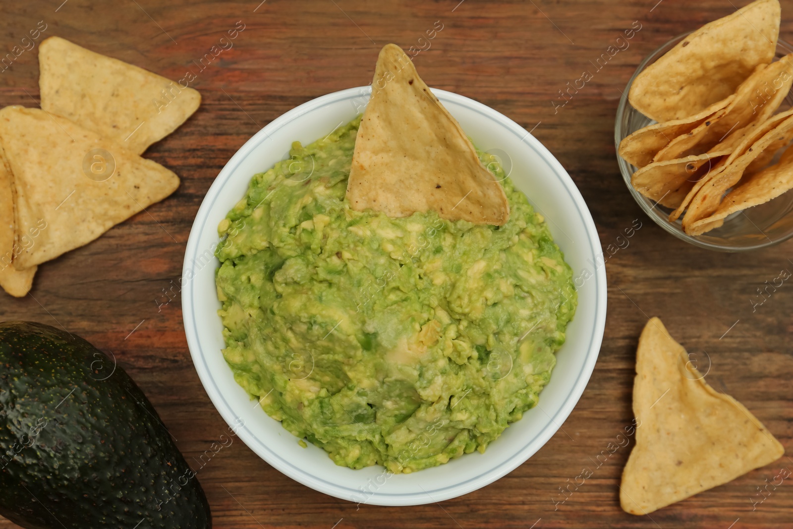 Photo of Delicious guacamole, avocado and nachos on wooden table, flat lay