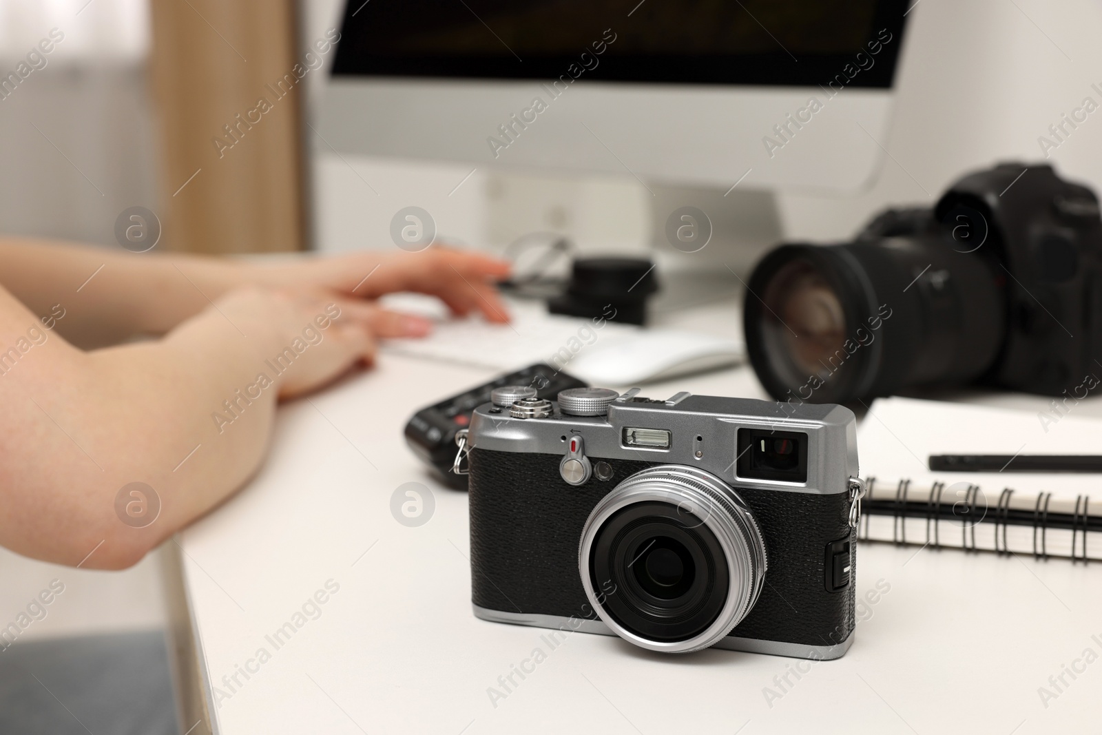 Photo of Photographer working on computer at white table with cameras indoors, closeup