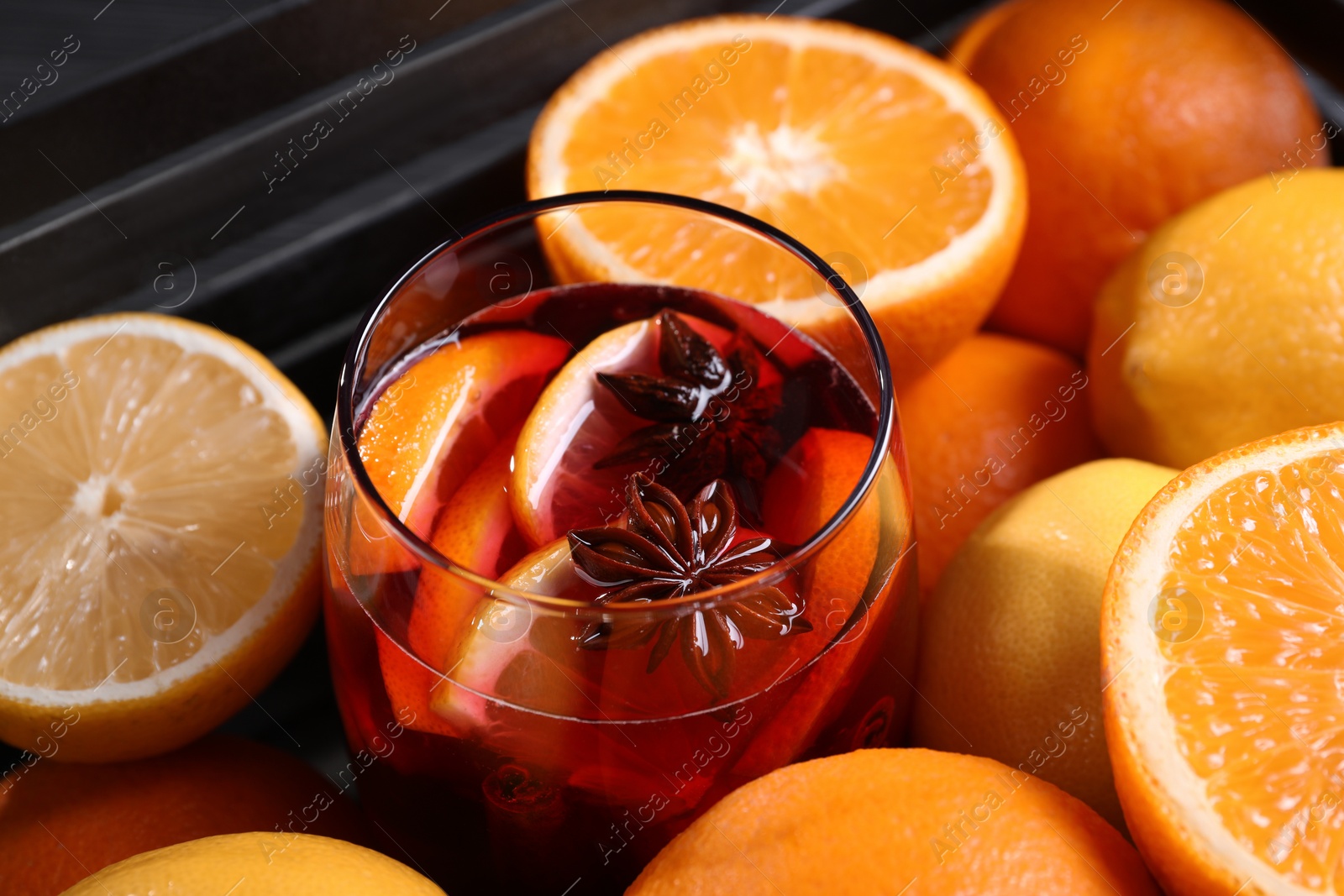 Photo of Glass of aromatic punch drink and fresh citrus fruits on table, closeup