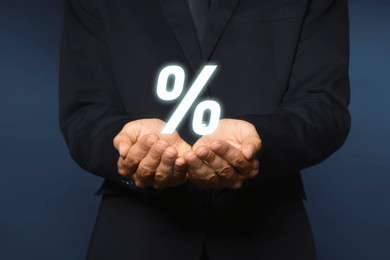 Image of Mortgage. Man holding percent sign on dark blue background, closeup