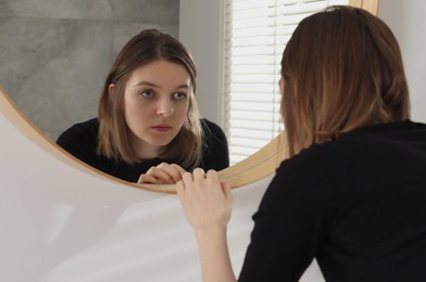 Photo of Sad young woman near mirror in room