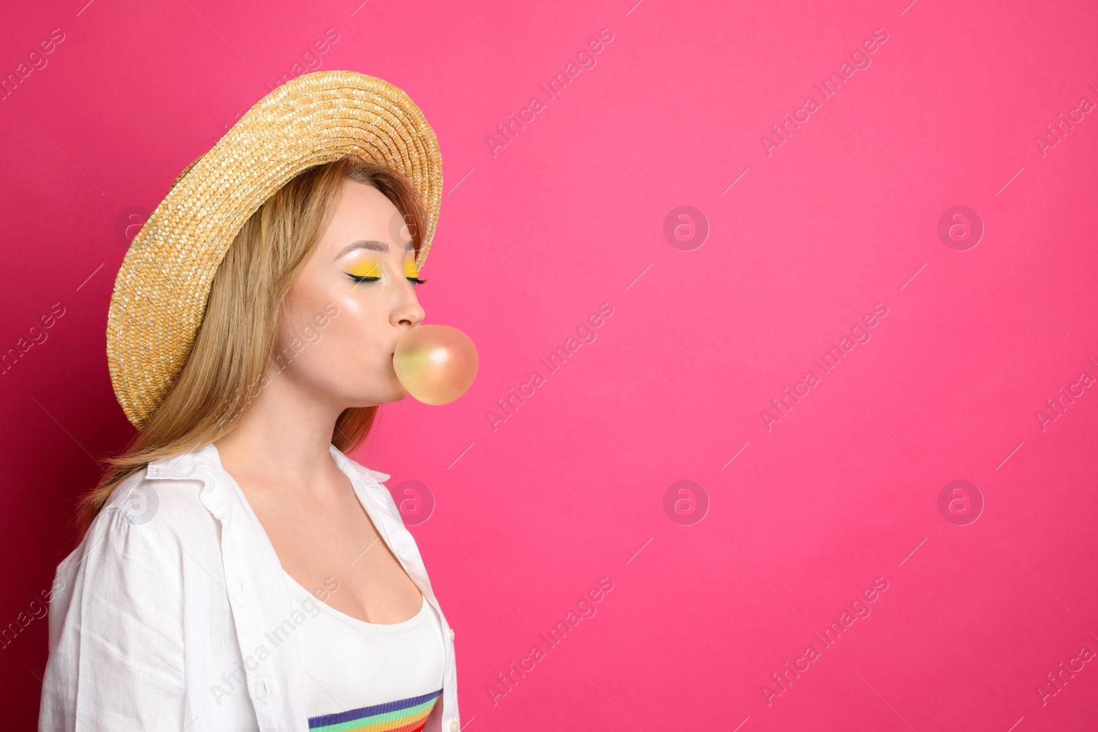 Photo of Fashionable young woman with bright makeup blowing bubblegum on pink background, space for text