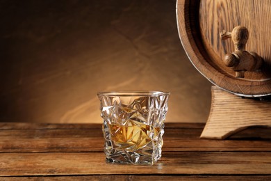 Photo of Glass of whiskey and wooden barrel on table, space for text