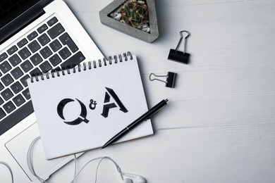 Photo of Notebook with text Q&A and laptop on white wooden table, flat lay