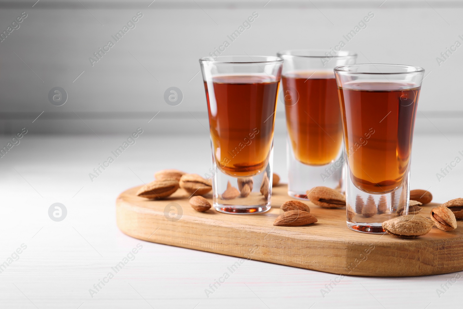 Photo of Shot glasses with tasty amaretto liqueur and almonds on white wooden table, closeup. Space for text