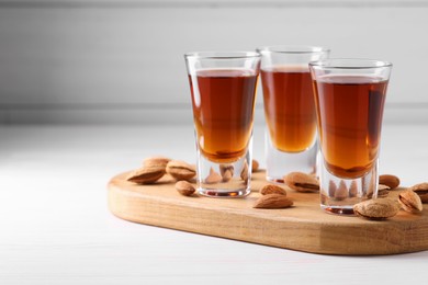 Shot glasses with tasty amaretto liqueur and almonds on white wooden table, closeup. Space for text
