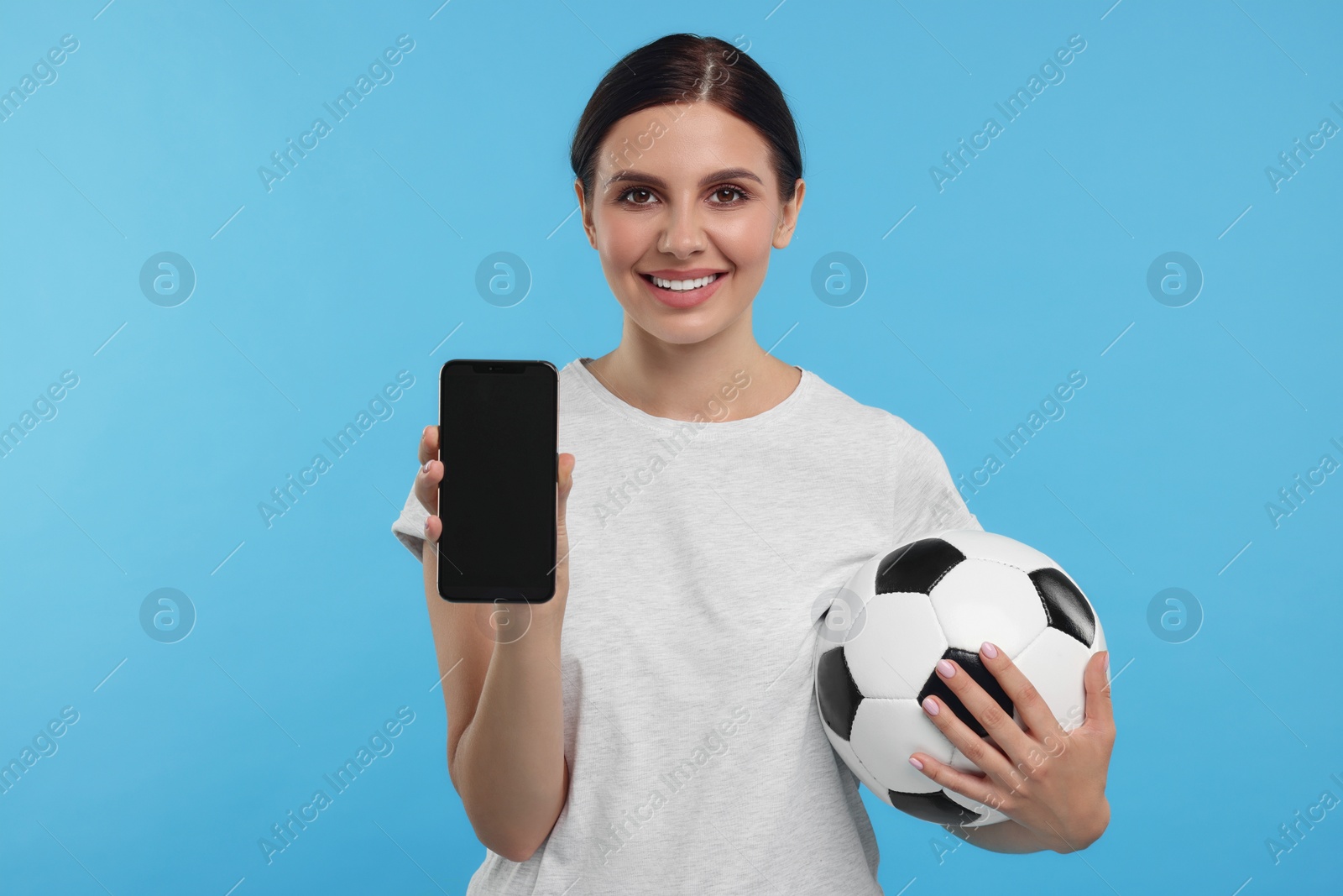 Photo of Happy sports fan with soccer ball and smartphone on light blue background