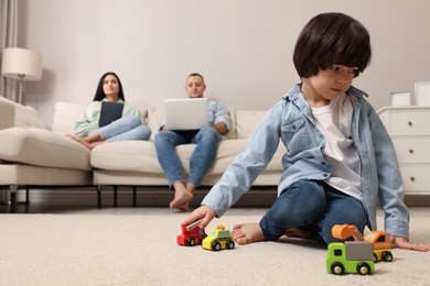 Photo of Sad child playing with toys and parents working at home