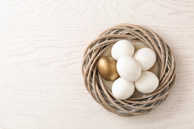 Photo of Golden egg among others in nest on wooden background, top view with space for text