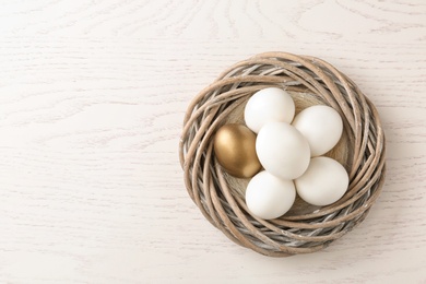 Golden egg among others in nest on wooden background, top view with space for text