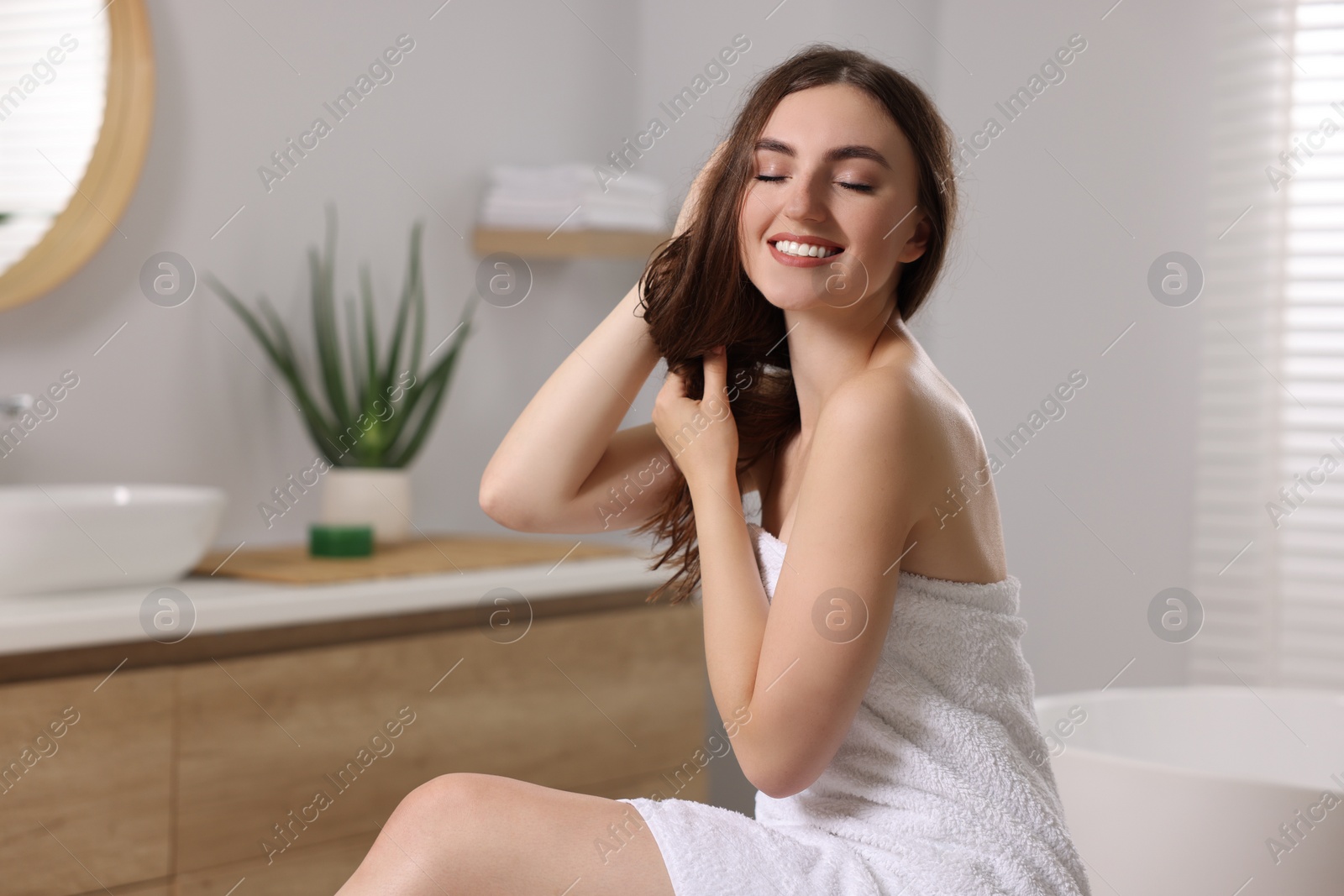 Photo of Young woman applying cosmetic hair mask in bathroom