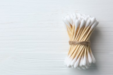 Photo of Many cotton buds on white wooden table, top view. Space for text