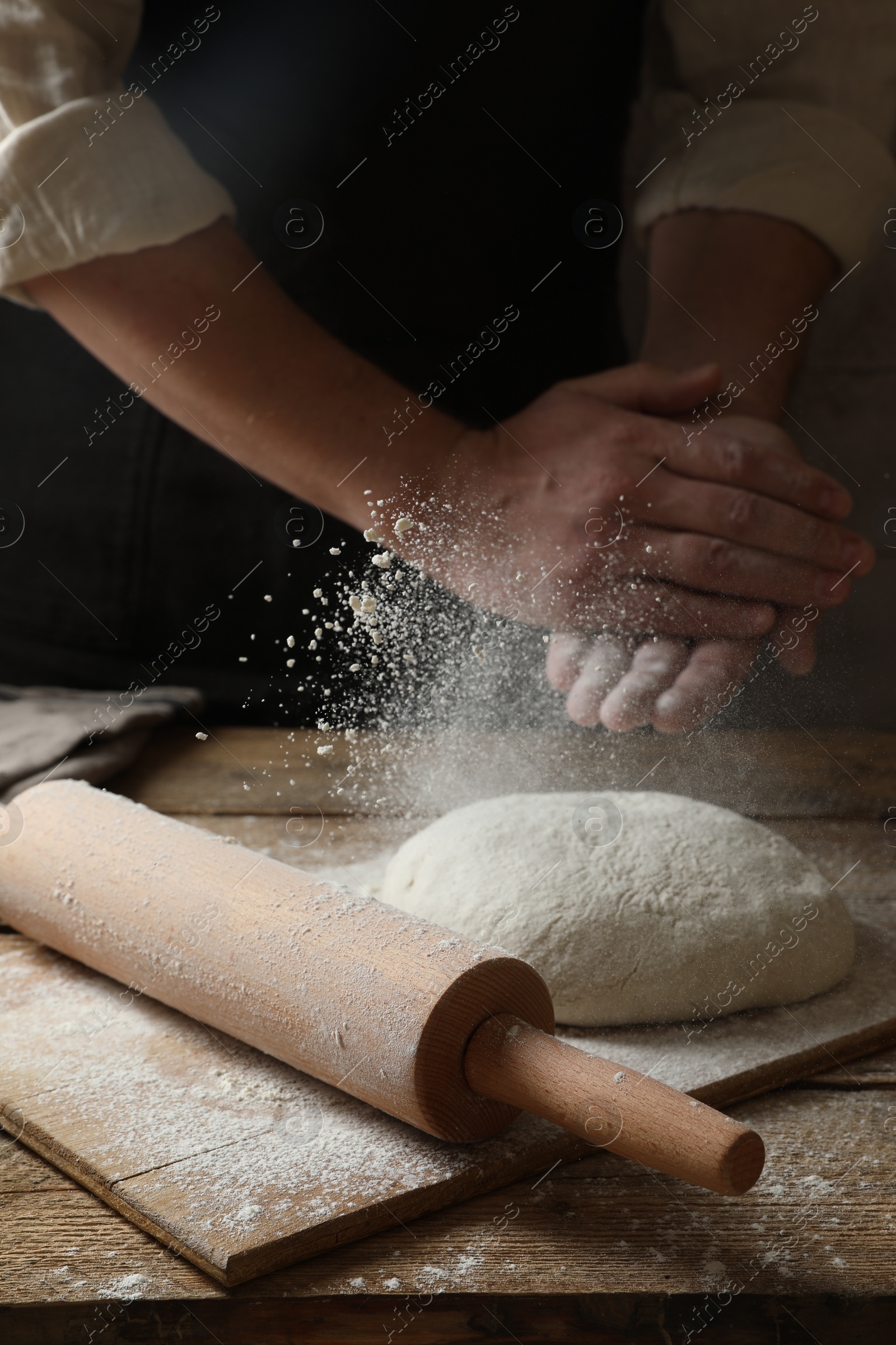 Photo of Man sprinkling flour over dough at wooden table, closeup