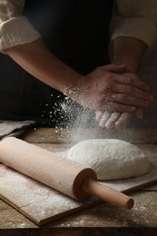 Man sprinkling flour over dough at wooden table, closeup