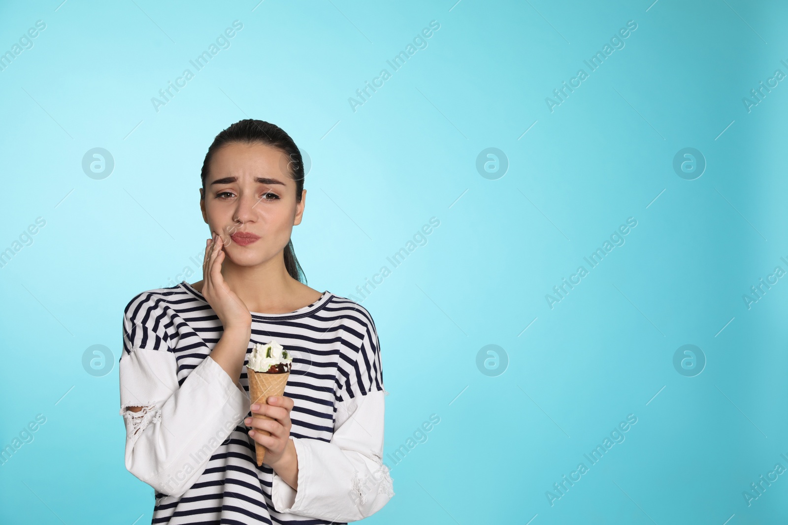 Photo of Emotional young woman with sensitive teeth and ice cream on color background. Space for text