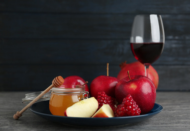 Photo of Honey, apples, pomegranate and glass of wine on grey table. Rosh Hashanah holiday