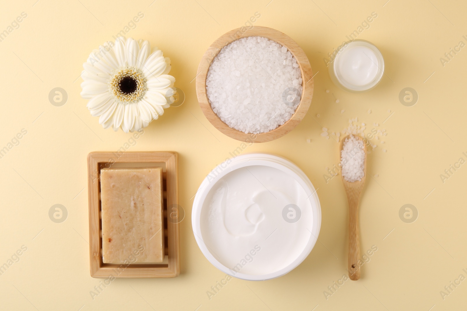 Photo of Jars of cream, body care products and gerbera flower on beige background, flat lay