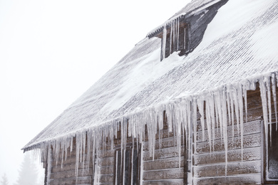Wooden house with icicles on snowy day. Winter vacation