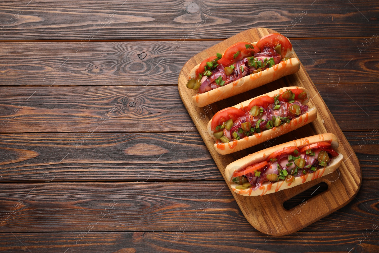 Photo of Tasty hot dogs with green onion, tomato, pickles and sauce on wooden table, top view. Space for text