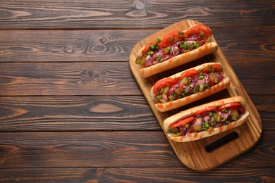 Photo of Tasty hot dogs with green onion, tomato, pickles and sauce on wooden table, top view. Space for text