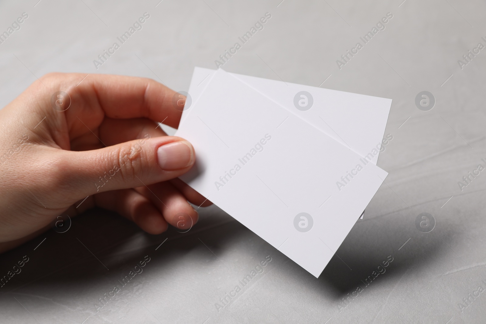 Photo of Woman holding blank cards at light grey table, closeup. Mockup for design