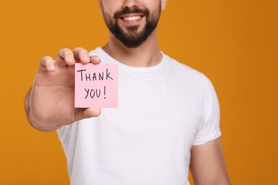 Photo of Man holding paper note with phrase Thank You on orange background, closeup