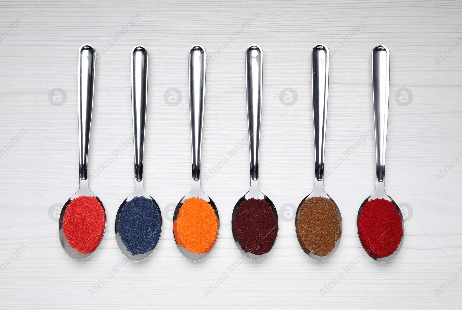 Photo of Spoons with different food coloring on white wooden table, flat lay