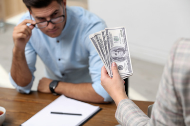 Woman offering bribe money to man at table