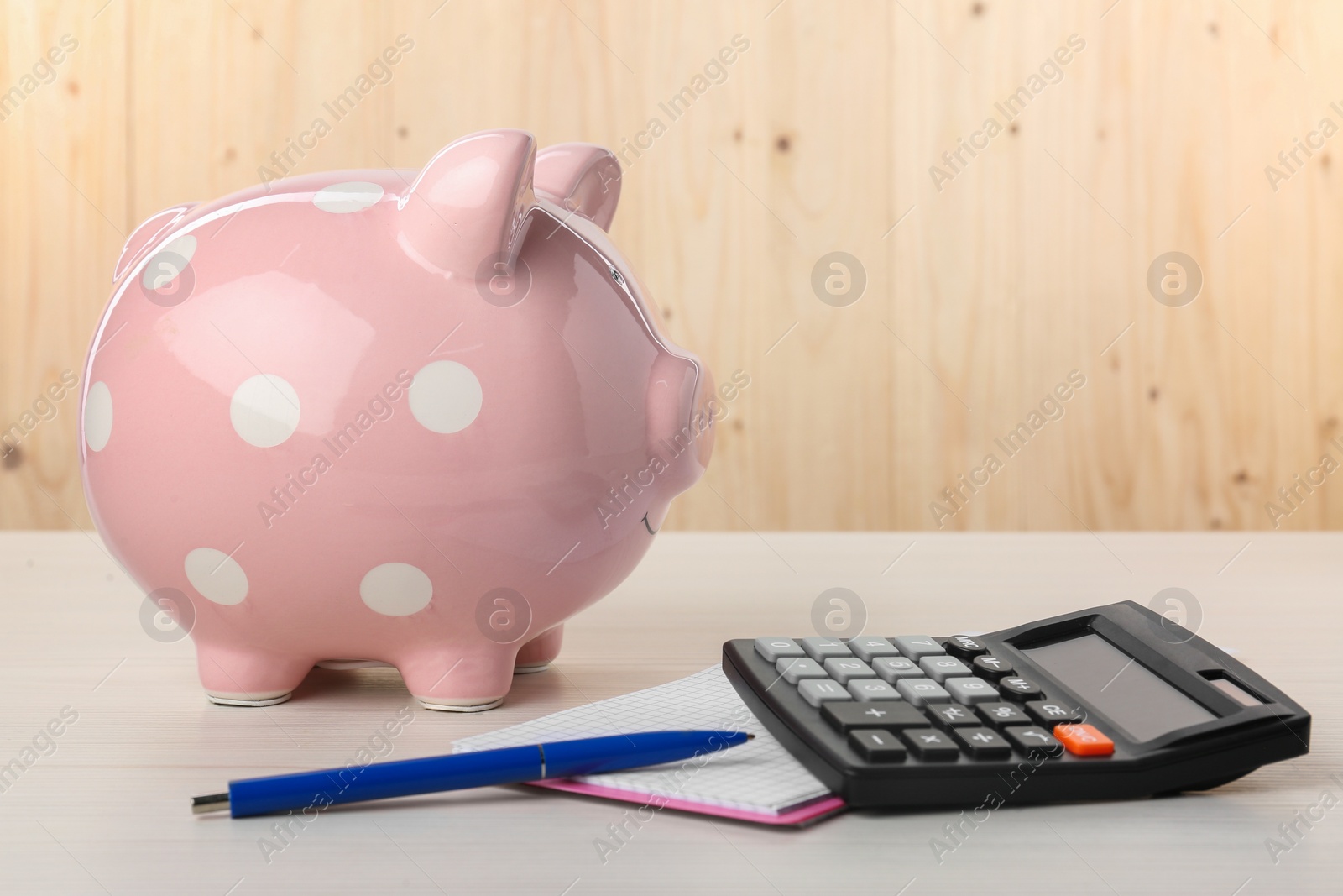 Photo of Calculator, notebook, pen and piggy bank on light wooden table