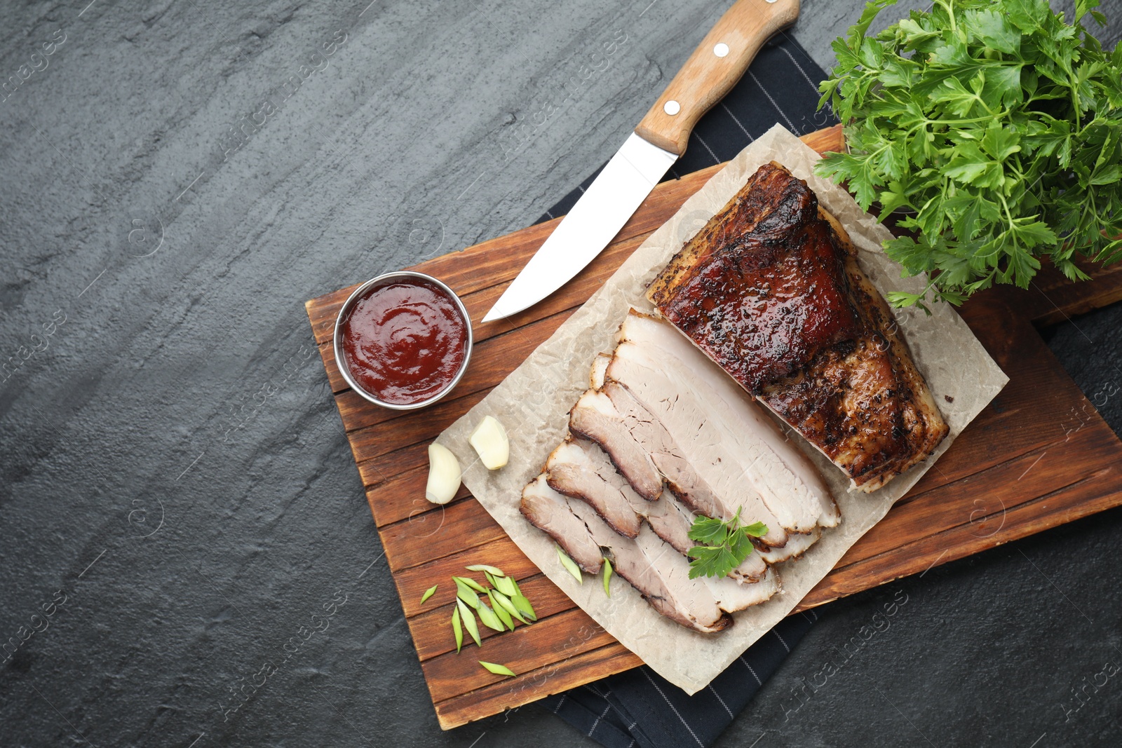 Photo of Pieces of baked pork belly served with sauce and parsley on black textured table, top view. Space for text