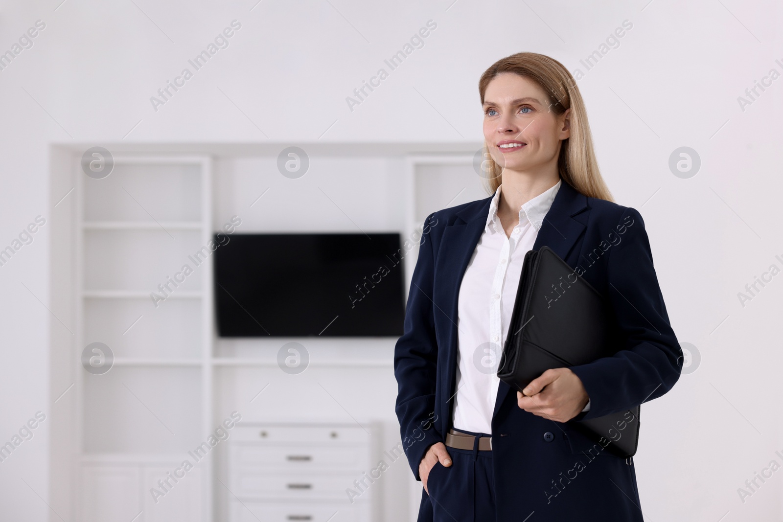 Photo of Happy real estate agent with leather portfolio indoors. Space for text