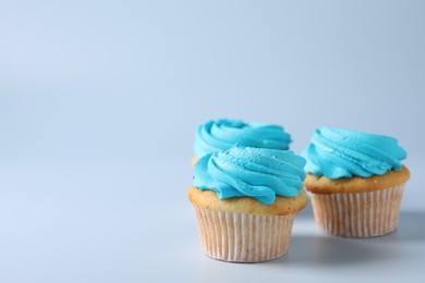 Delicious cupcakes with bright cream on light blue background, space for text