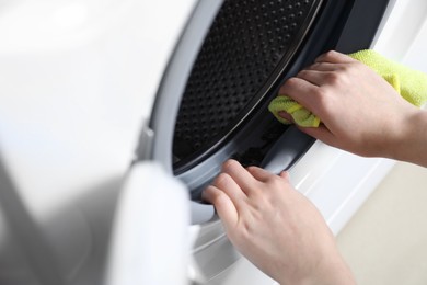 Photo of Woman cleaning washing machine with rag, closeup