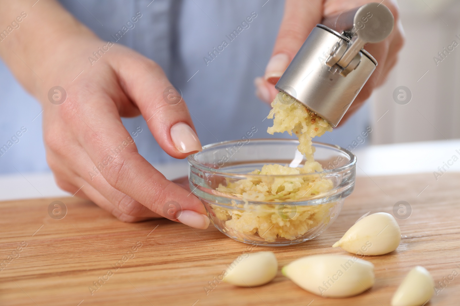 Photo of Woman squeezing garlic with press at wooden table, closeup