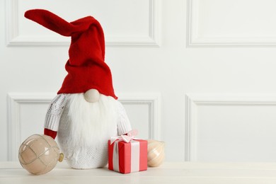 Cute Christmas gnome, gift box and festive balls on white wooden table. Space for text