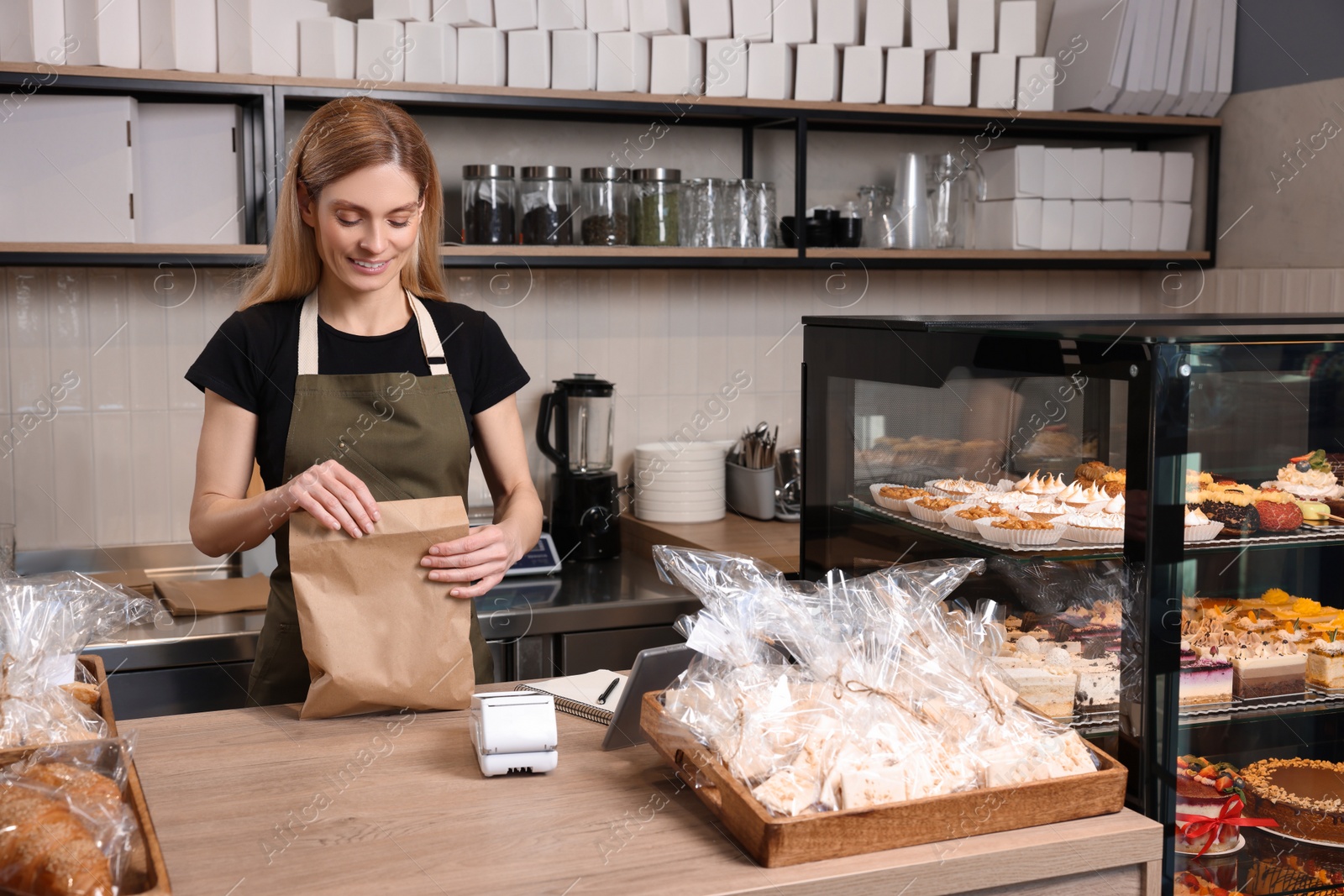 Photo of Happy seller with paper bag at cashier desk in bakery shop