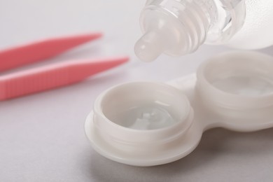 Photo of Dripping solution into case with contact lenses on white background, closeup