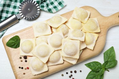 Photo of Uncooked ravioli with basil and peppercorns on white wooden table, flat lay