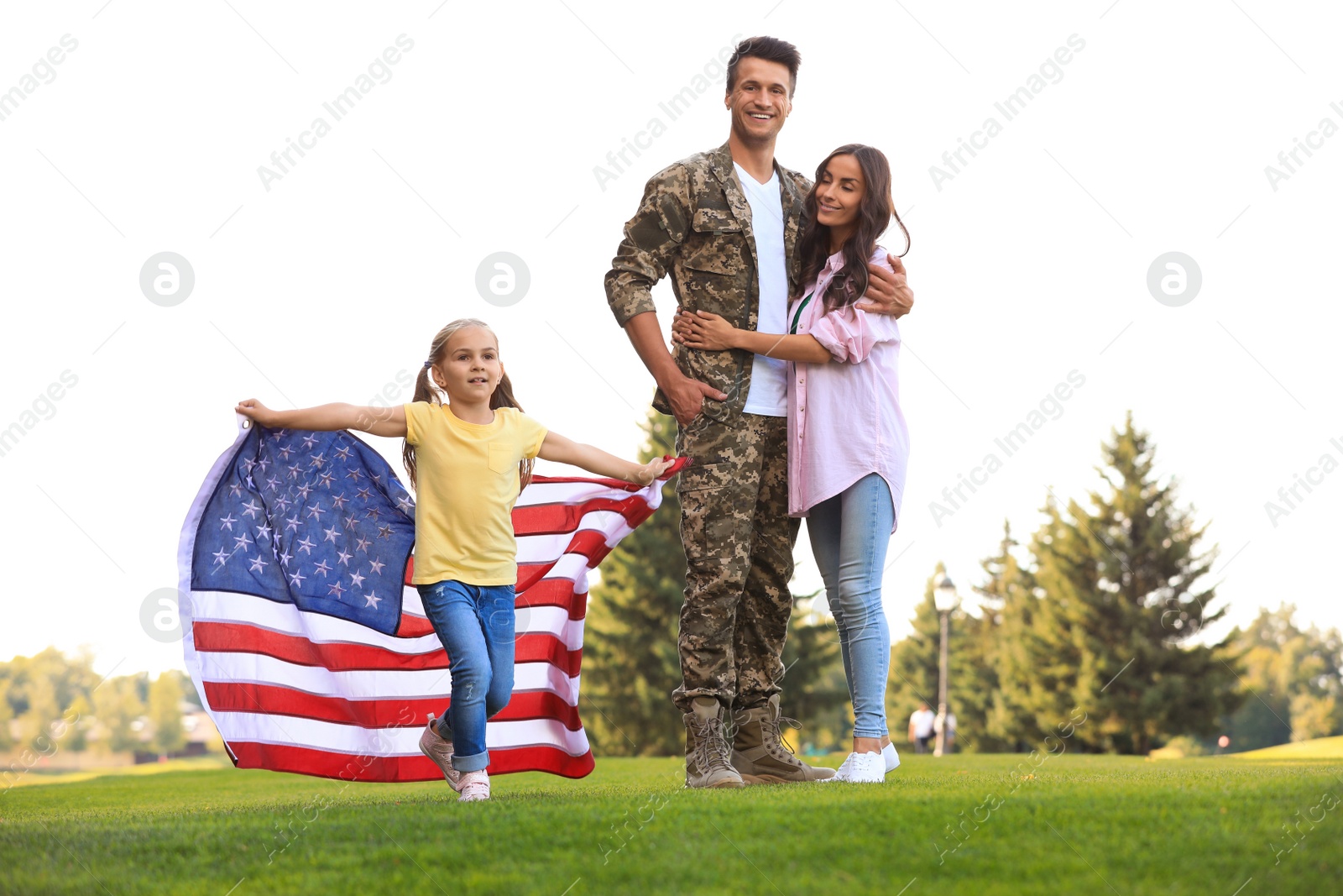 Photo of Little girl running with American flag, her father in military uniform and mother at sunny park